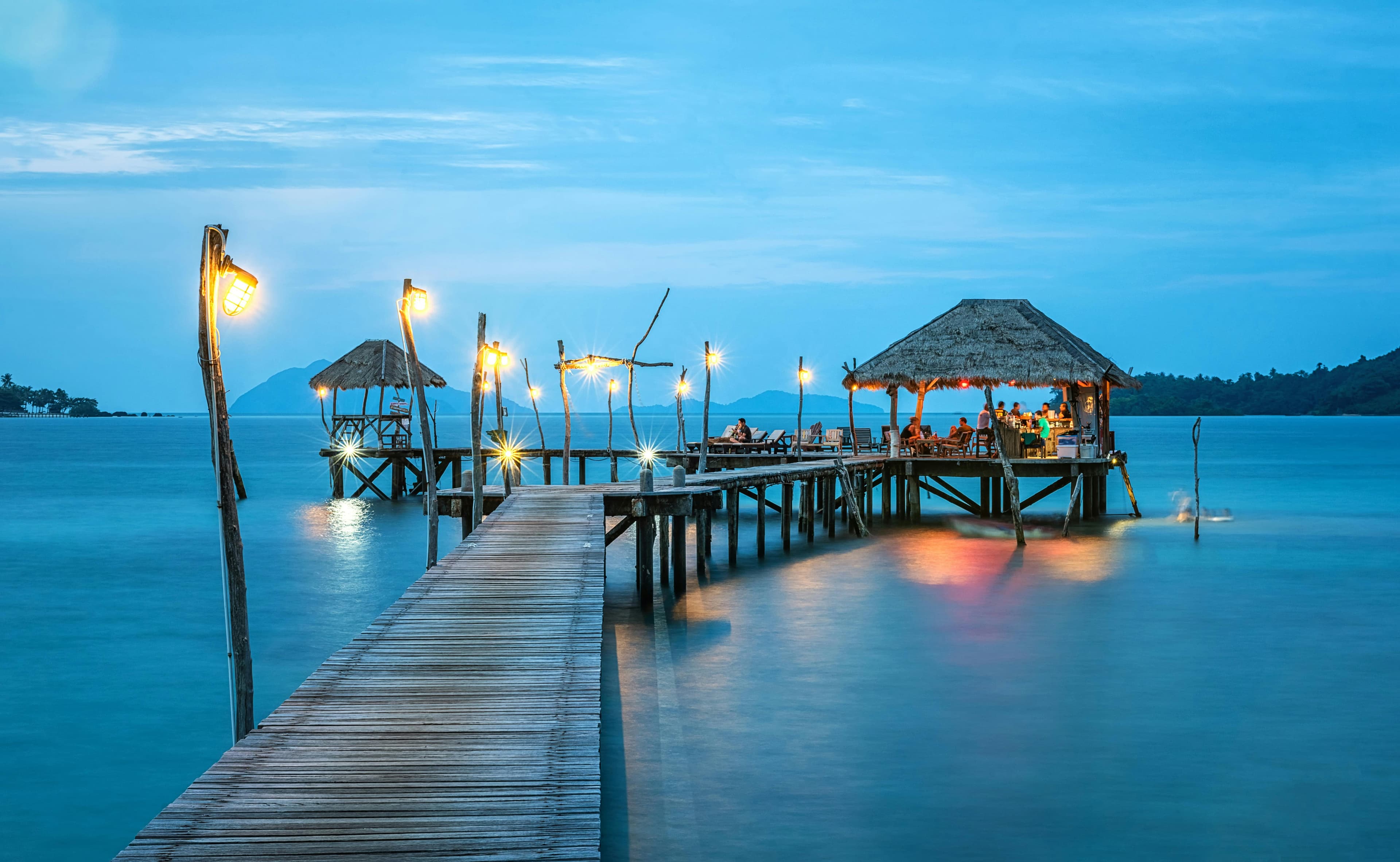 A beautiful wooden pier and resort over calm ocean water at sunset.